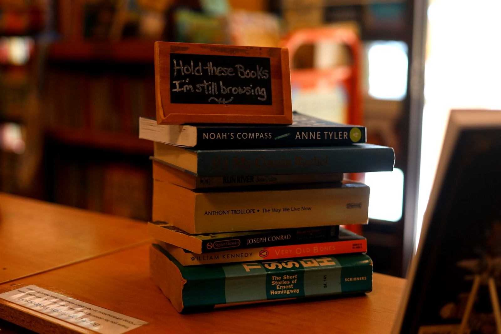 A stack of used books topped with a handwritten sign reading "Hold these books, I'm still browsing" at the Book Nook